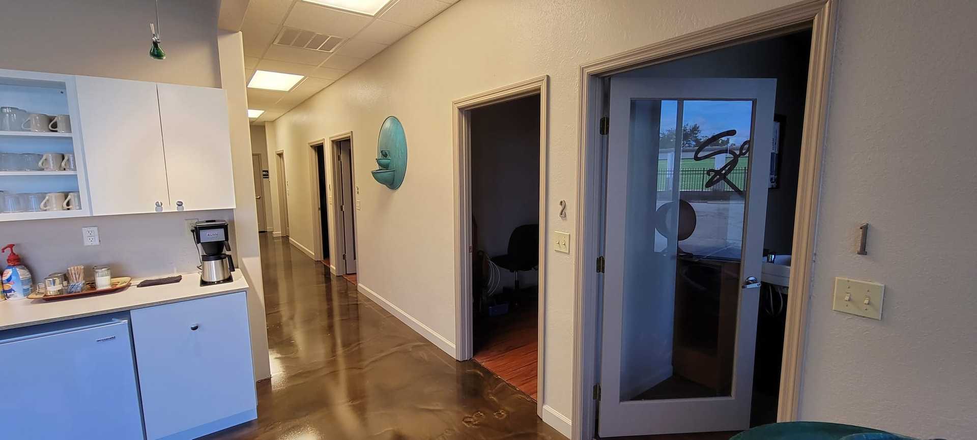 Hallway with polished floor, several open doors, and a coffee station on the left.